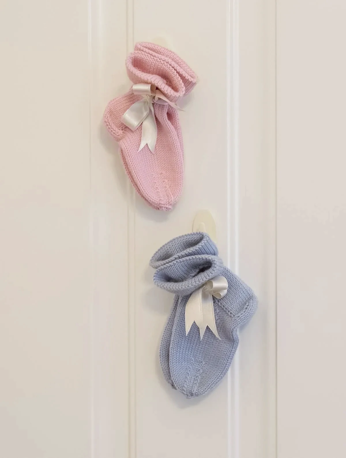 Zarte gestrickte Babysocken in Rosa und Blau mit Satinschleife an der Tür